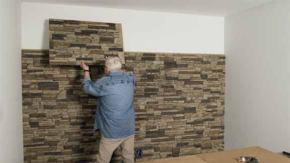 Man installs faux stone panels up on wall 