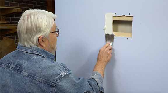 Man puts joint compound on a hole in the wall
