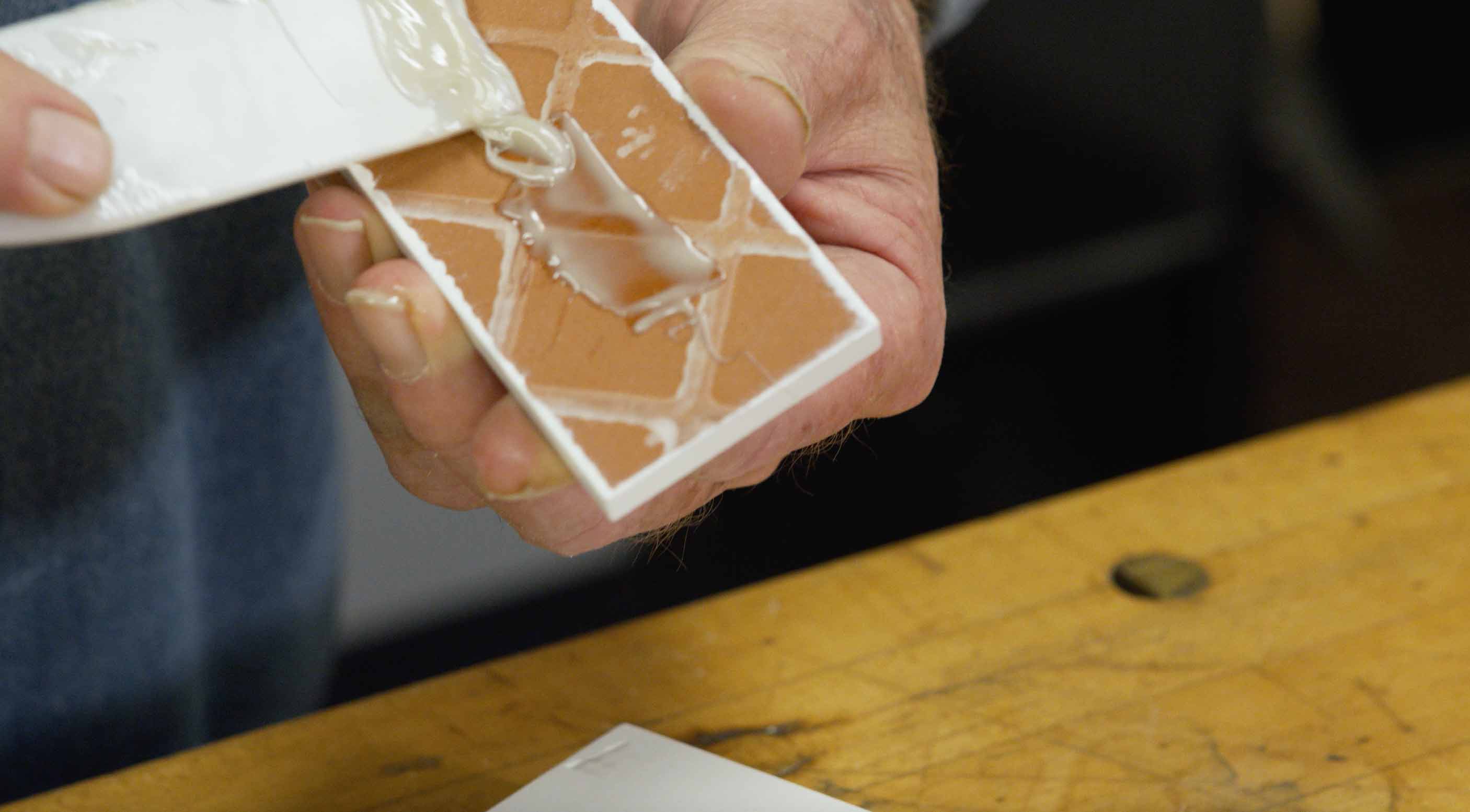 Man spreads epoxy on back of ceramic tile