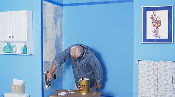 Man uses adhesive to adhere shower panel to wall