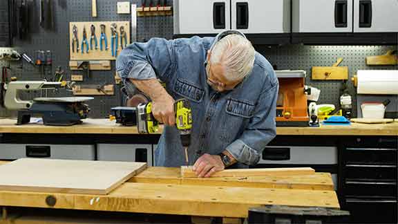 Man uses hand drill to attach wooden block to wood