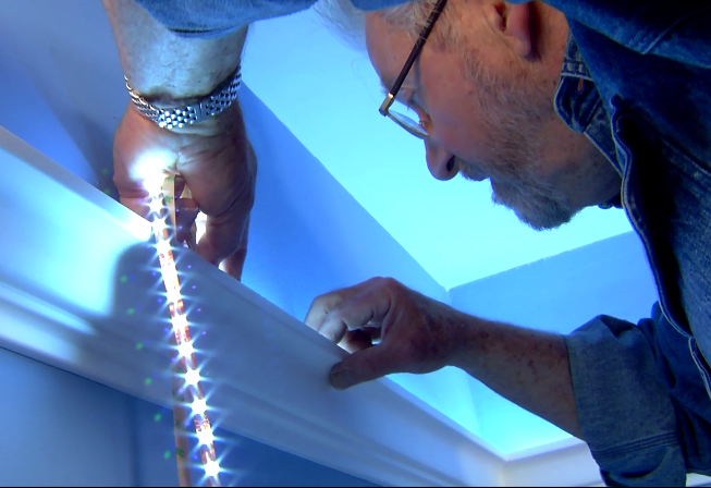 Man placing LED lights behind crown molding to create cove lighting 