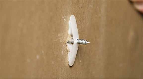 The backside of a wall board with a toggle wall anchor